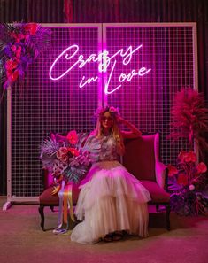 a woman is sitting on a chair in front of a neon sign that says beauty in love