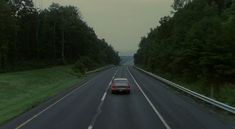 a car is driving down the road in front of some tall trees and green grass