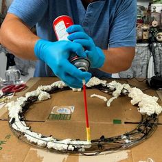 a man in blue gloves is painting a wreath with white foam and glue on it