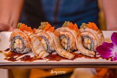 sushi rolls on a white plate with sauce drizzled over them and an orchid in the foreground