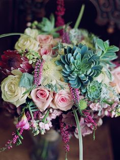 a vase filled with flowers and greenery on top of a wooden table next to a mirror