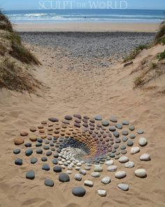 there is a circle made out of rocks on the sand at the beach with water in the background