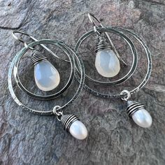 Two tiny genuine freshwater pearls are carefully wrapped in sterling silver wire. The white pearls dangle from sterling silver rings which I have formed, soldered, and hammered by hand. Inside the rings are natural Chalcedony teardrops. The earrings dangle from handformed Sterling Silver earwires. The silver has been oxidized and polished to create the patina finish. Be sure to see all photos and video for size and color reference. Total Earring Length: About 2 inches White Teardrop Wire Wrapped Pearl Earrings, White Teardrop Wire Wrapped Earrings, Silver Teardrop Pearl Earrings With Ear Wire, Sterling Silver Teardrop Dangle Earrings With Pearl Drop, Sterling Silver Teardrop Pearl Earrings With Charm, Pearl White Teardrop Sterling Silver Earrings, Handmade Drop Pearl Earrings In Sterling Silver, Handmade Sterling Silver Drop Pearl Earrings, Wire Wrapped Teardrop Pearl Jewelry