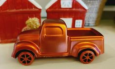 an orange toy truck sitting on top of a table next to two red tin buildings