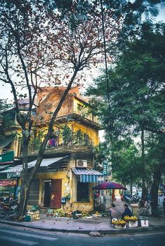 an old yellow building sitting on the side of a road next to trees and people