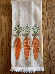 three carrots on a white dish towel hanging from a wooden table with tassels