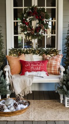 a porch with christmas wreaths and pillows on the front door bench next to pine cones