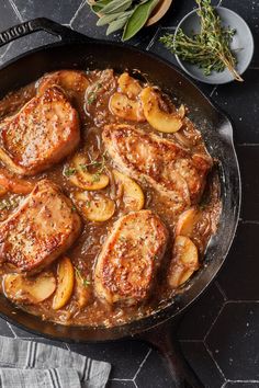 pork chops and potatoes are in a skillet on the table next to some herbs