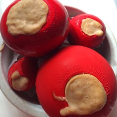 three red balls in a white bowl with peanut butter on top, and the bottom one is brown