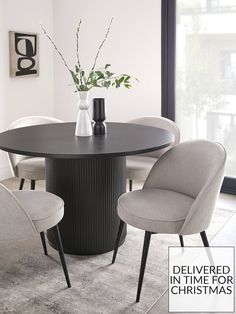 a round dining table with four chairs around it and a vase on the table top