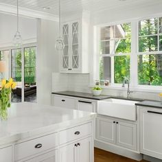 a kitchen with white cabinets and black counter tops is pictured in this image, there are yellow flowers on the window sill