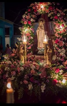 an altar with candles and flowers on it in front of a virgin mary statue at night