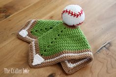 a crocheted hat with a baseball on top sits on a wooden table next to a ball