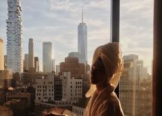 a woman in a headscarf looks out the window at skyscrapers and buildings