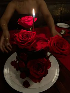 a man is sitting at a table with a cake decorated with red roses and a lit candle