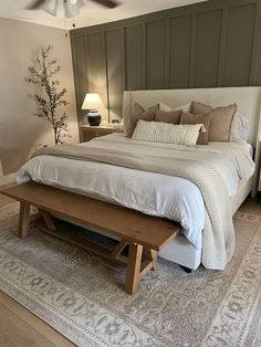 a bedroom with a large bed and wooden bench in the middle, along with two lamps on either side of the bed