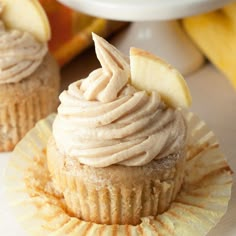 two cupcakes with frosting and apple slices on top are sitting next to each other