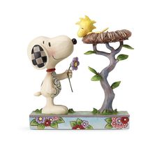 a snoopy figurine holding a flower next to a tree with a bird on it