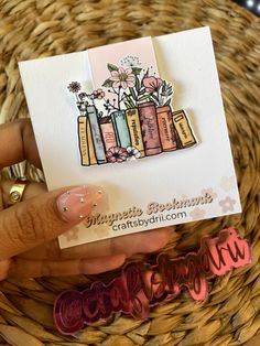 a hand holding a card with flowers in vases on it next to a basket