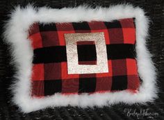 a red and black plaid pillow with white fur on the bottom that has a gold square in the center