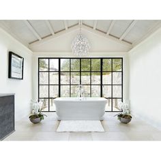 a white bath tub sitting under a chandelier in a bathroom next to a window