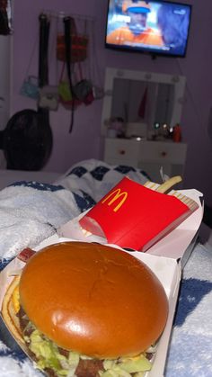 a large hamburger sitting on top of a bed next to a red box with a mcdonald's sign