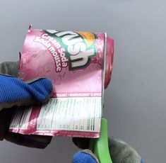 a person wearing blue gloves holding up a pink and green bag of ice - cream