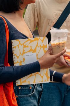 a woman holding a plastic cup in her hand while standing next to another person with an orange and white bag