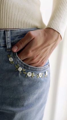 a woman wearing jeans with flowers on the side and her hand in her pocket,