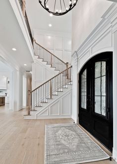 an entryway with stairs and a rug on the floor in front of a black door