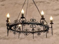 a chandelier with five lit candles hanging from it's center, in front of a stucco wall