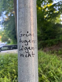 graffiti on the side of a pole in front of some grass and trees with cars behind it