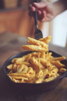 a person holding a fork full of macaroni and cheese in a black bowl