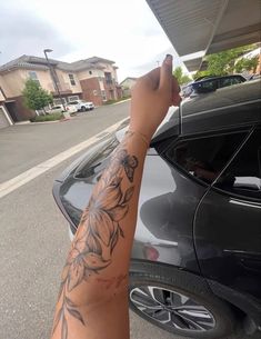 a person with tattoos on their arm next to a black car and some houses in the background