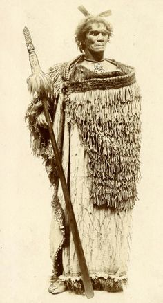 an old black and white photo of a man dressed in native american garb holding a stick