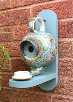 a blue shelf with a birdhouse on it next to a brick wall and potted plant