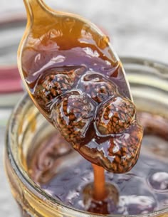 a spoon full of liquid sitting on top of a glass jar filled with honey syrup