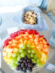 a platter filled with grapes, apples and other fruit on a table next to a basket of cookies