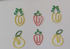 four different colored paper clips in the shape of pineapples and peppers on a white surface