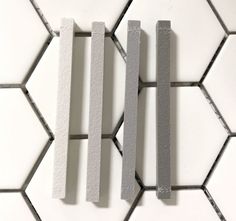 three pieces of white and grey tile on a wall with hexagonal tiles in the background