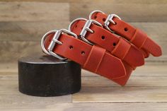 four orange leather belts with metal buckles on top of a wooden table next to a black object