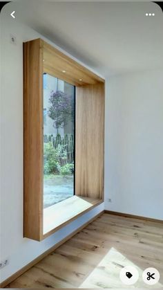 an empty room with wooden floors and a window in the corner that looks out onto a garden