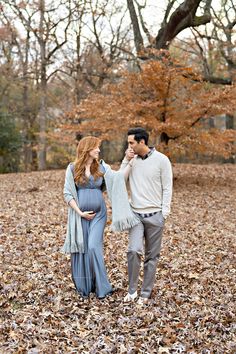 a pregnant couple walking through leaves in the woods