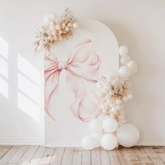 an arch decorated with balloons and flowers in the shape of a bow on a white wall