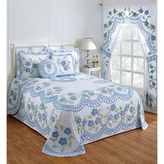 a white bed with blue flowers on it in a bedroom next to a large window