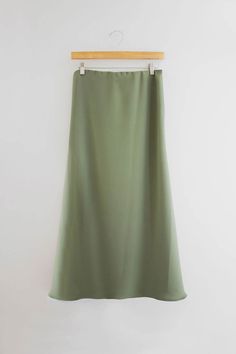 an olive green skirt hanging on a white wall with a wooden hanger in front of it