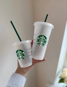 two starbucks cups with green straws in their hands