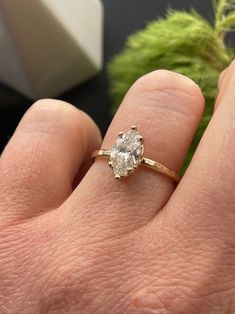 a woman's hand with a diamond ring on top of her finger and a plant in the background