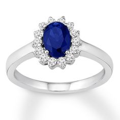 an oval blue sapphire and diamond ring on a white background with the center stone surrounded by small diamonds