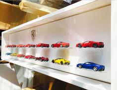 a display case filled with lots of toy cars on top of a white shelf next to a window